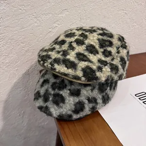 Deux bérets à motif léopard empilés sur une table en bois avec un mur texturé