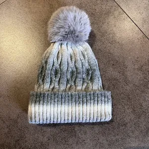 Détail macro du bonnet en tricot gris dégradé avec texture côtelée et pompon en fourrure
