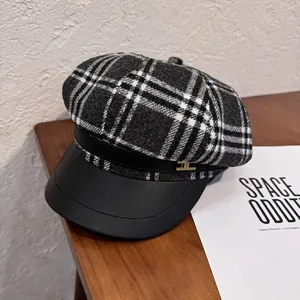 Detail of grey plaid newsboy cap featuring black visor and gold metal logo accent