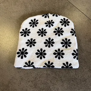 Detailed top view of a white knitted beanie featuring black floral patterns and soft texture