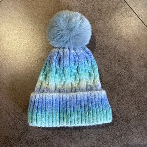 Vue détaillée d'un bonnet en tricot dégradé bleu et vert avec un pompon en fausse fourrure