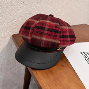 Detail of red plaid newsboy cap with black leather brim and golden metal badge