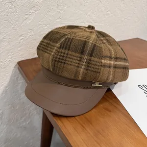 Detail of brown plaid newsboy cap showing wool texture and gold metal buckle on wood