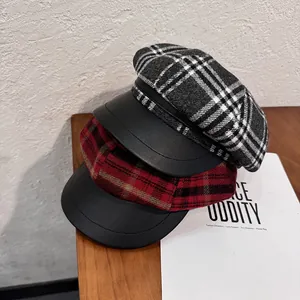 Fashionable red and grey plaid newsboy caps with leather brim on wooden desk