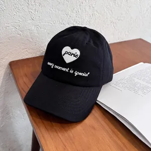 Close-up of black canvas baseball cap with white heart embroidery and Paris text detail