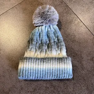 Détail du tricot torsadé épais et du pompon en fourrure grise sur le bonnet dégradé
