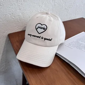 Detailed close-up of cream cotton baseball cap with black Paris heart embroidery