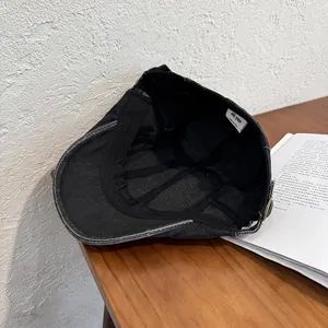 Detail of vintage black cotton beret showing metal buckle and brand wash label on wood table