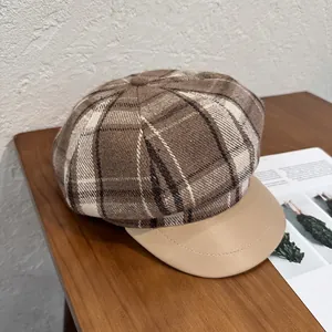 Detail of brown plaid wool fabric and beige faux leather brim on a vintage newsboy cap