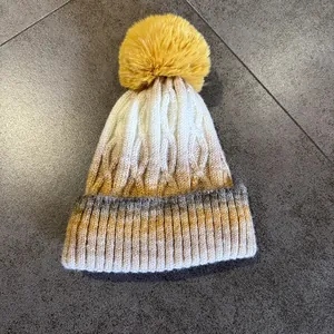 Détail du bonnet en maille dégradée avec motif torsadé et pompon en fausse fourrure jaune