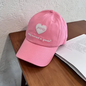 Detail of pink cotton baseball cap with white heart embroidery and slogan on wood background
