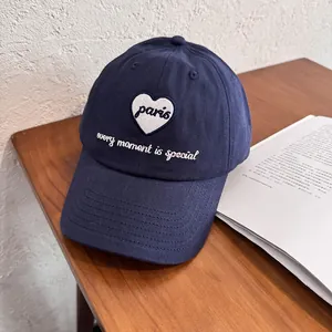 Detail of navy blue cotton cap featuring white heart embroidery and Paris text on wood