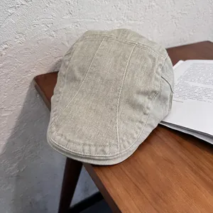 Detail of light khaki newsboy cap showing twill fabric texture on a wooden desk
