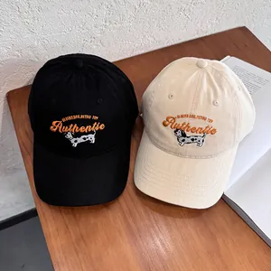 Dettaglio del ricamo con bassotto e scritte su cappellini da baseball in cotone nero e beige