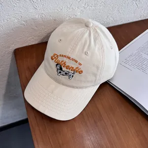 Dettaglio del berretto in tela beige con ricamo di un cucciolo e scritte in stile retrò