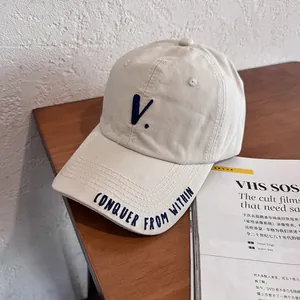Detail of beige baseball cap featuring blue 'V' embroidery and slogan on brim