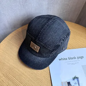 Detail of grey denim camper cap featuring brown leather patch and metal ring embellishment