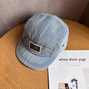 Detail of light blue denim camp cap with square logo patch and metal ring accent