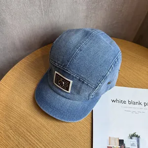Detail of blue denim 5-panel camper hat with brown leather patch and metal ring