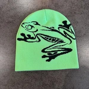 Dettaglio di un berretto in maglia verde neon con motivo jacquard a rana nera su fondo