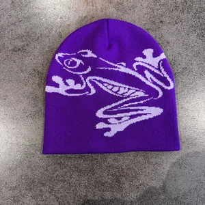 Dettaglio ravvicinato di un berretto viola in maglia con motivo jacquard a rana bianca