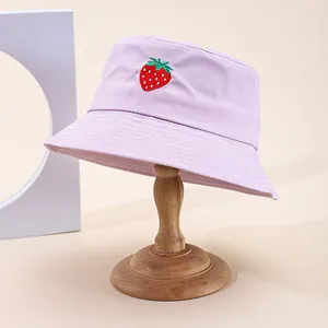 Lilac bucket hat with strawberry embroidery on a wooden stand against a beige backdrop