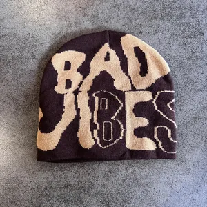 Detailed close-up of dark brown knit beanie featuring beige jacquard Bad Vibes lettering