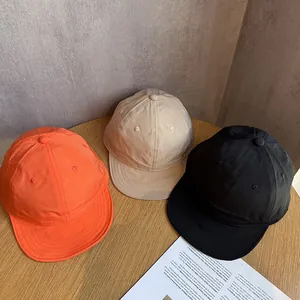 Three minimalist short brim outdoor baseball caps in orange, beige, and black colors