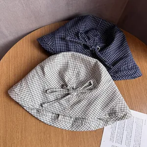 Detail of navy and cream plaid sun hats with bow accents and metal eyelets on wood