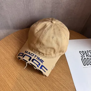 Detailed close-up of blue MADTIME embroidery and distressed edges on khaki canvas baseball cap