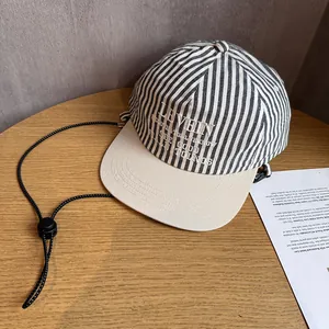 Detail of striped baseball cap with embroidery and adjustable windproof cord on wood
