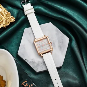 Vue détaillée d'une montre carrée en or rose avec bracelet blanc sur marbre