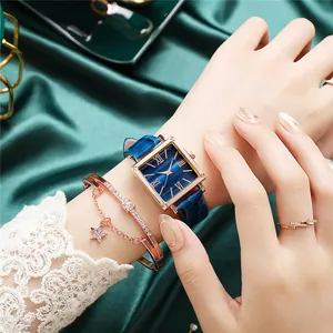 Gros plan d'une montre carrée cadran émeraude avec bracelet bleu et bijoux dorés