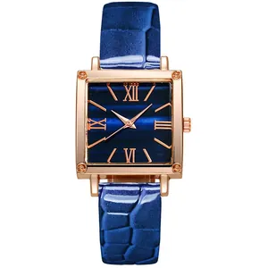 Détail d'une montre carrée or rose avec bracelet en cuir bleu et chiffres romains