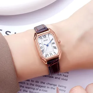 Rectangle rose gold watch with brown crocodile leather strap and blue hands on wrist