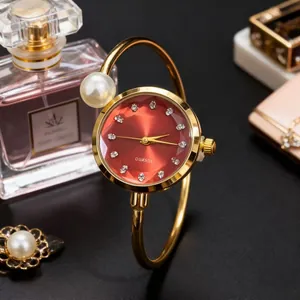 Détail d'une montre bracelet dorée à perles avec cadran rouge et index en cristaux
