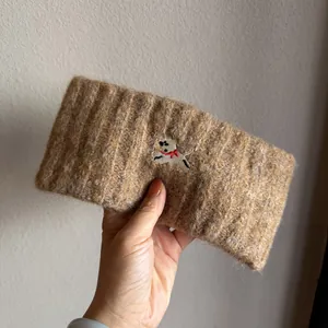 Close-up of a warm brown knitted headband with detailed puppy embroidery and thick texture