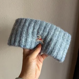Detalle de diadema de punto azul claro con bordado de perrito blanco y lazo rojo