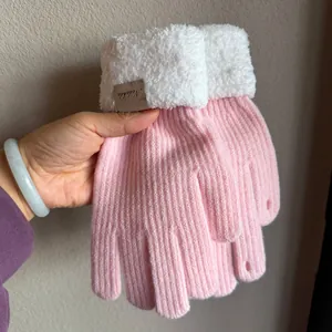 Detail of pink knitted gloves featuring soft white faux fur cuffs and leather tag detail