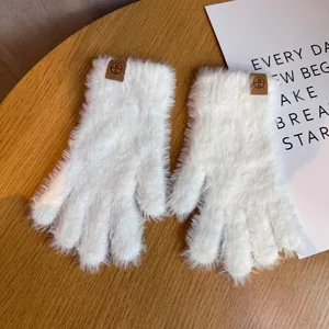 Détail de gants d'hiver en peluche blanche avec étiquette logo en cuir sur table en bois