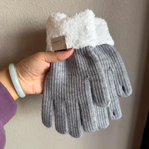 Detail of gray knitted glove with white faux shearling cuff and brown leather patch