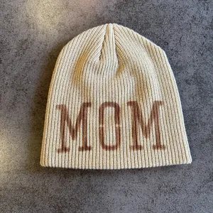 Dettaglio del berretto in maglia beige con scritta MOM marrone e trama a coste