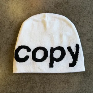 Close-up of white knit beanie with black woven letters on a dark textured background