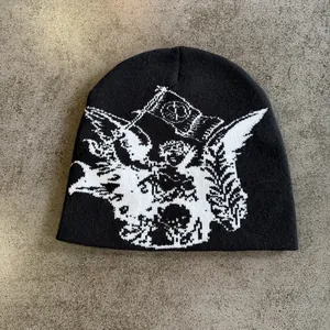 Detail van de zwarte gebreide muts met wit engelenpatroon op grijze stenen achtergrond
