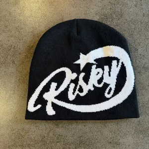 Detail of black knit beanie featuring white Risky jacquard text and star pattern
