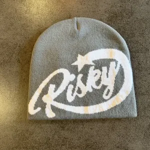 Detail of grey knit beanie featuring white jacquard Risky lettering and star pattern