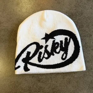 Close-up of white knitted beanie featuring black jacquard Risky letter pattern details