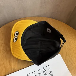 Detail of yellow cotton cap showing cartoon eye embroidery and internal adjustable strap