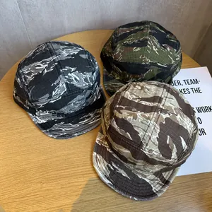 Three multi-color camouflage five-panel camper hats displayed on a light wooden table