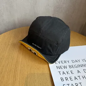 Close-up of black cotton baseball cap with yellow brim and embroidered cartoon eyes